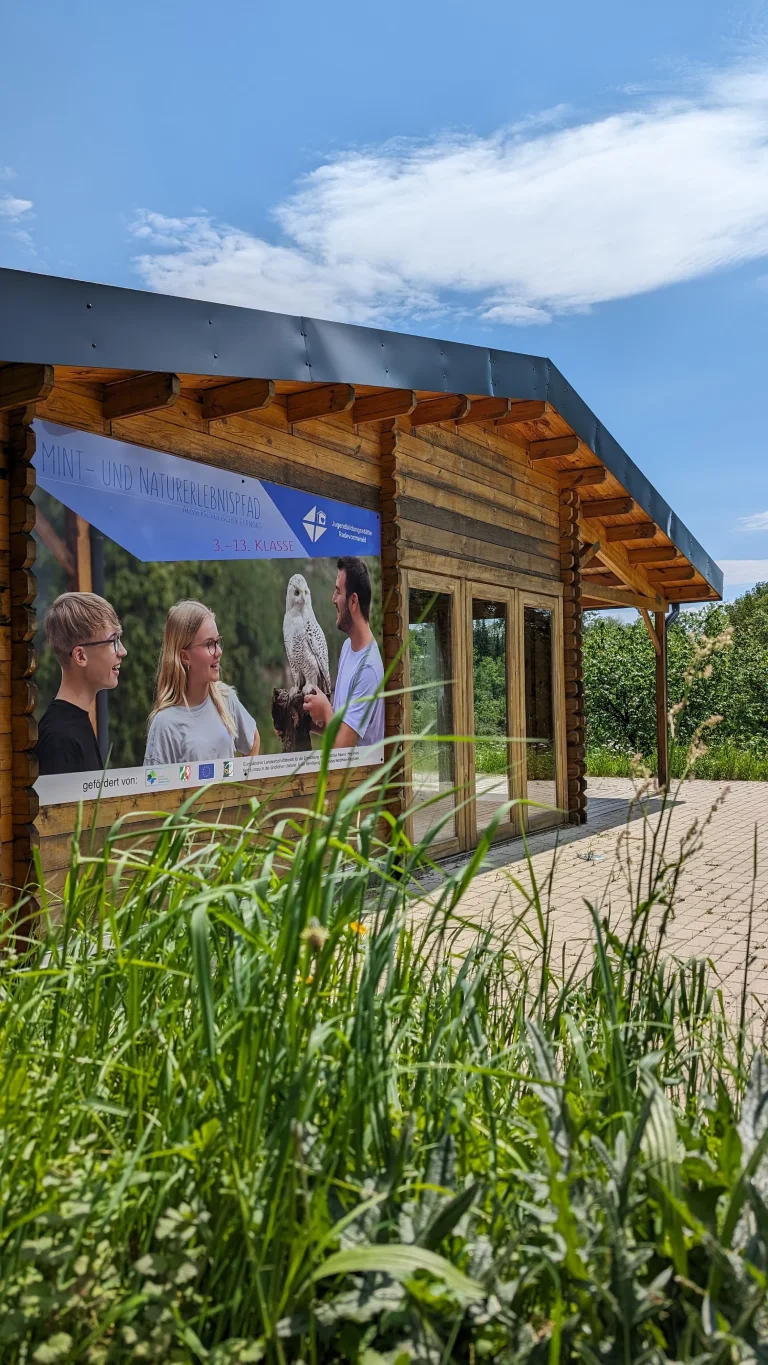 Holzgebäude mit großer Fensterfront und sichtbaren Personen im Inneren in naturnaher Umgebung – Evangelische Gesellschaft für Deutschland KdöR