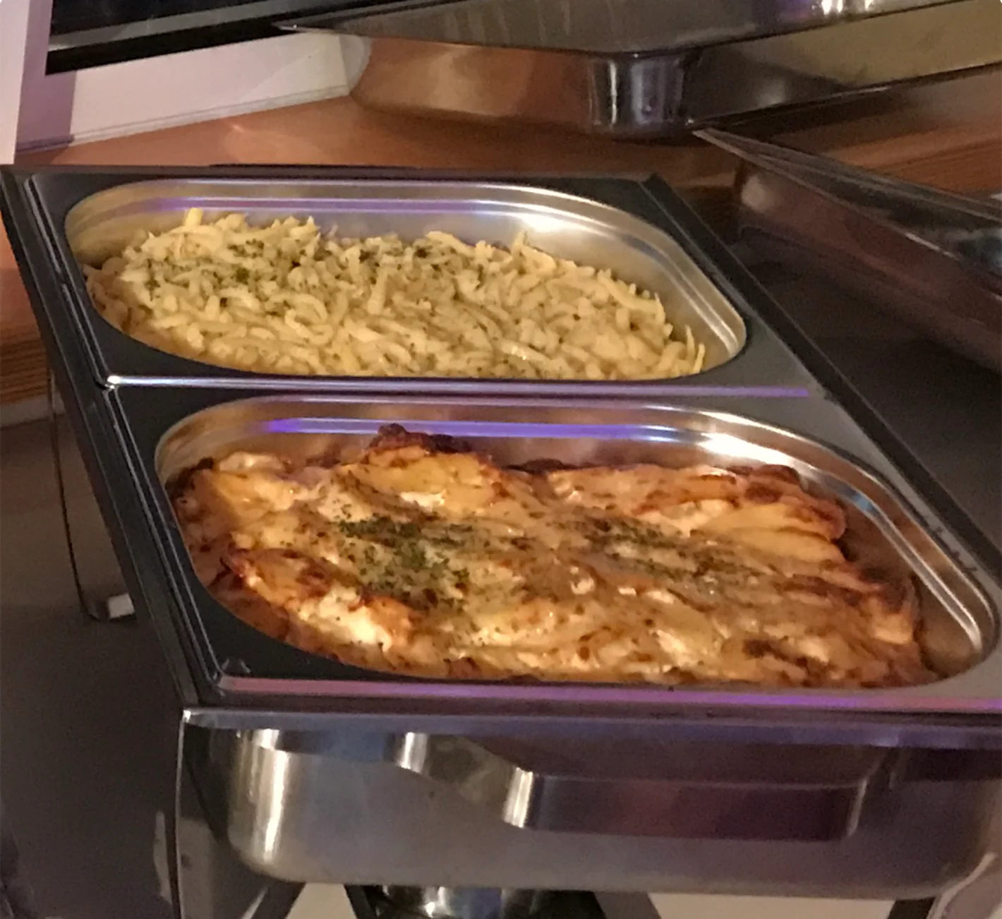 Buffet mit warmen Speisen, darunter Nudeln und ein Auflauf in Edelstahlbehältern – Evangelische Gesellschaft für Deutschland KdöR