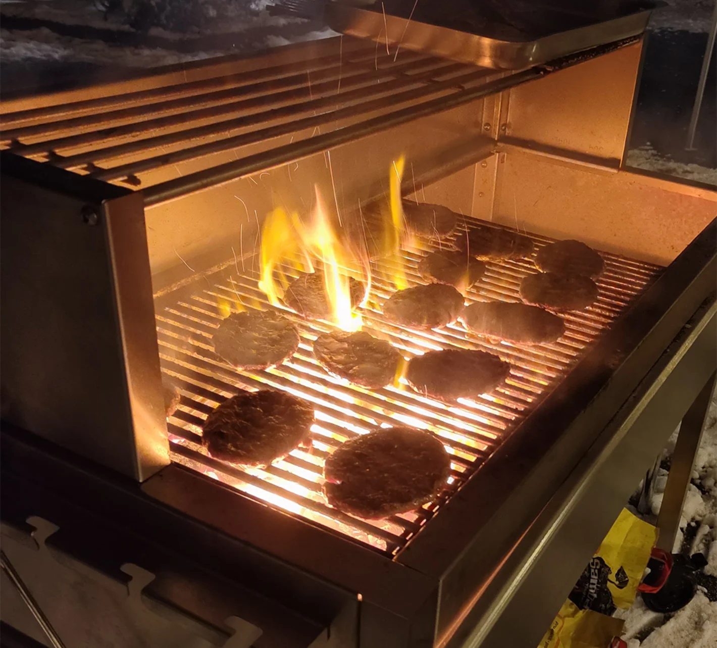 Grill mit offenen Flammen und mehreren Burger-Patties auf dem Rost – Evangelische Gesellschaft für Deutschland KdöR