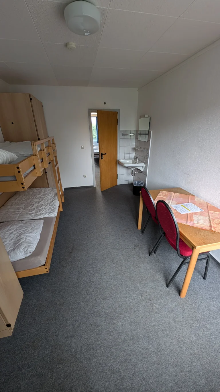 Kleines Zimmer mit Etagenbett, Tisch, Stühlen und Tür im Hintergrund – Evangelische Gesellschaft für Deutschland KdöR