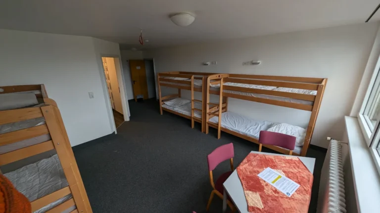 Mehrbettzimmer mit Etagenbetten, Tisch und Stühlen in einfacher Ausstattung – Evangelische Gesellschaft für Deutschland KdöR